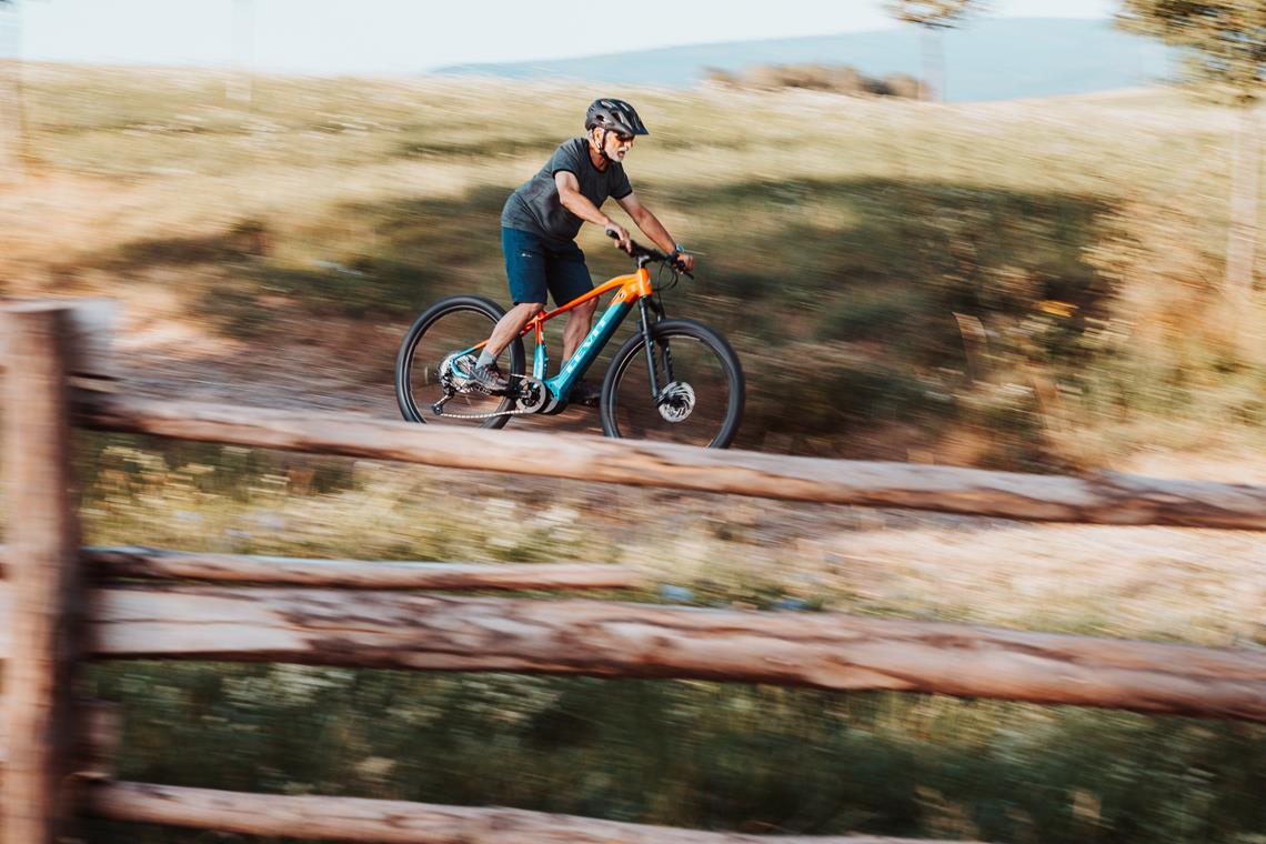 Mężczyzna w sile wieku jedzie na rowerze elektrycznym polną drogą.